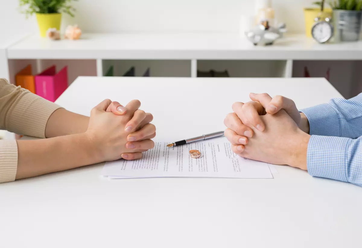 Acte necesare divorț în 2023 - mâinile unui cuplu aflat față în față, alături de acte și verighetele