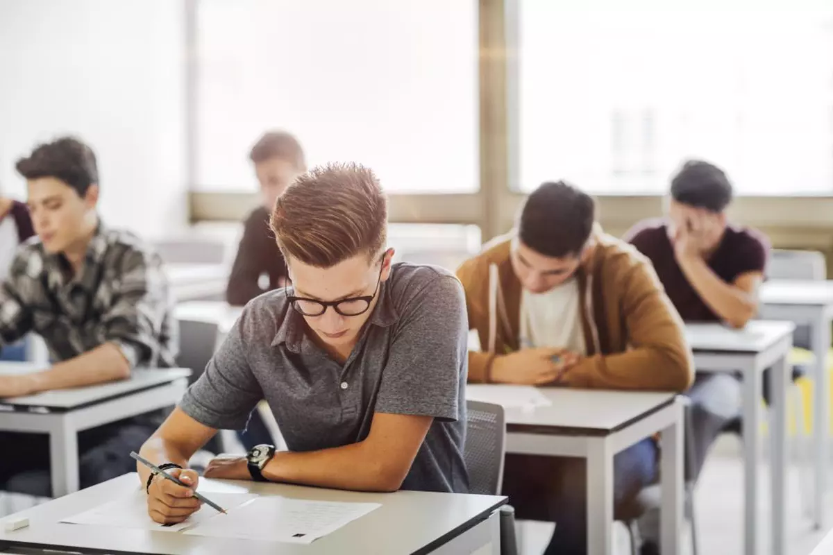 Calendarul anului şcolar 2022-2023 pentru fiecare judeţ - grup de elevi de liceu la un examen în sala de clasă.