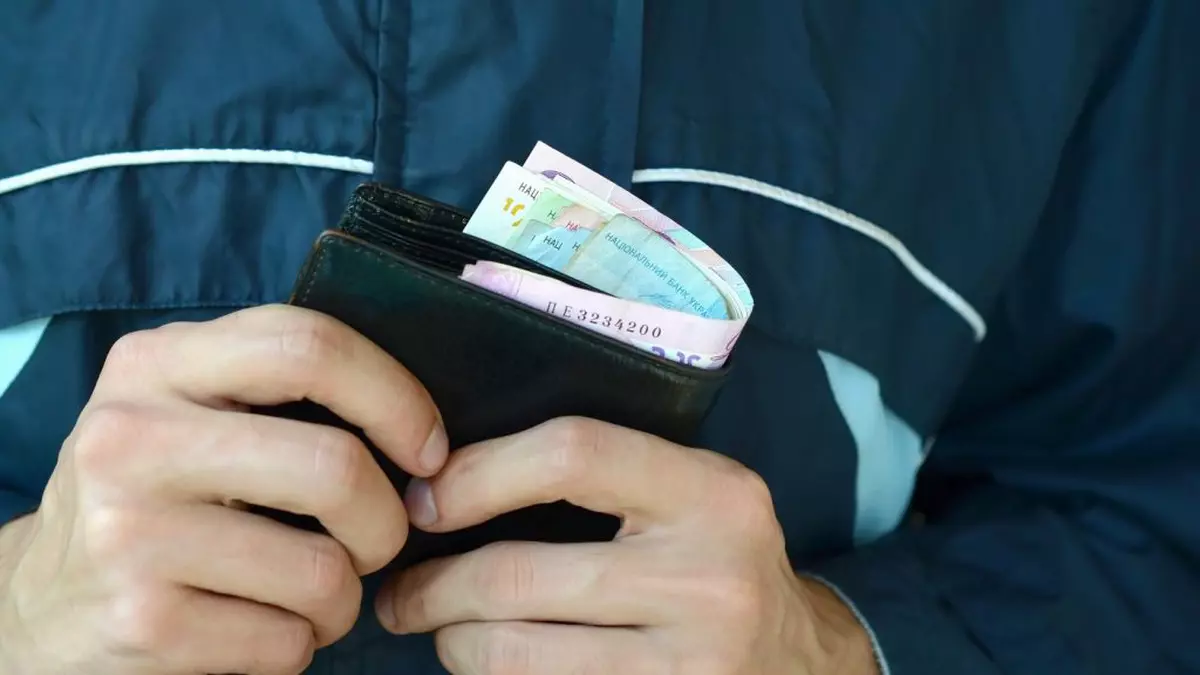 barbat care tine in maini un portofel negru de piele plin de bancnote