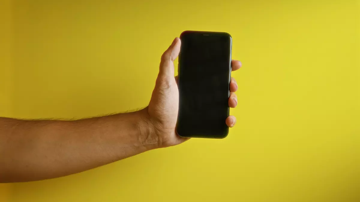 Telefoane sub 1.000 de lei la eMAG de Black Friday 2024 - Imagine cu un smartphone ţinut de o mână de bărbat pe un fond galben