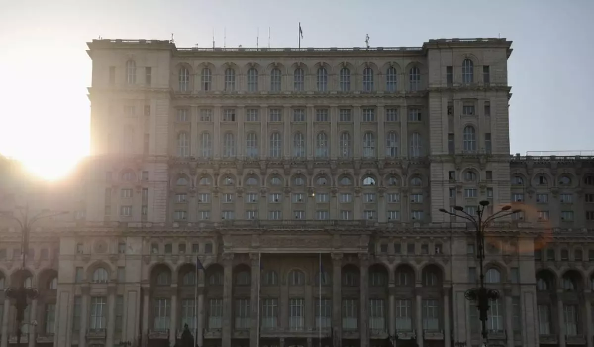 Prim plan cu Palatul Parlamentului din București, cu soarele care strălucește puternic în colțul din stânga-sus al clădirii