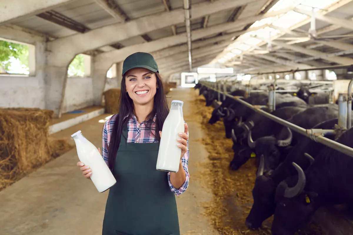 Lapte de bivoliţă – Ce proprietăţi şi beneficii are - Imagine cu o tânără fermieră care ţine în mâini două sticle cu lapte de bivoliţă