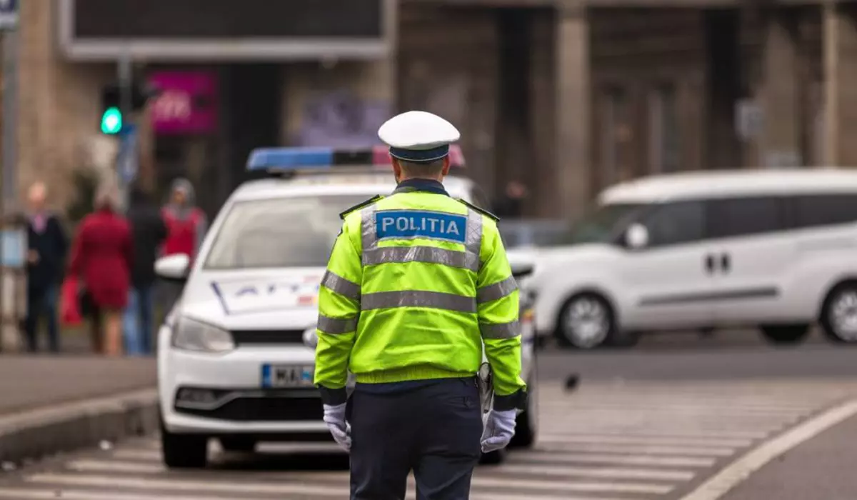 agent politie imbracat in uniforma pe fundal masina de politie