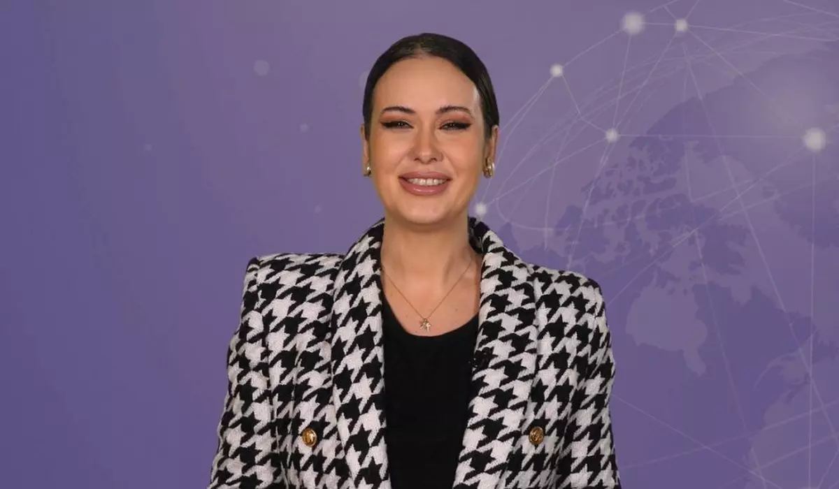 Denisa Macovei, gazda rubricii 5 știri by Libertatea - Monden, pe fundal mov, îmbrăcată cu un sacou în pătrățele albe și negre