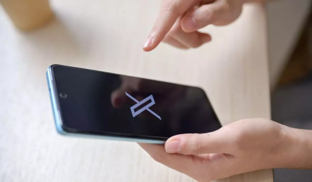 O imagine în prim plan a unei mâini de femeie care ține un smartphone cu logo-ul X pe ecran la o masă în interior. social media