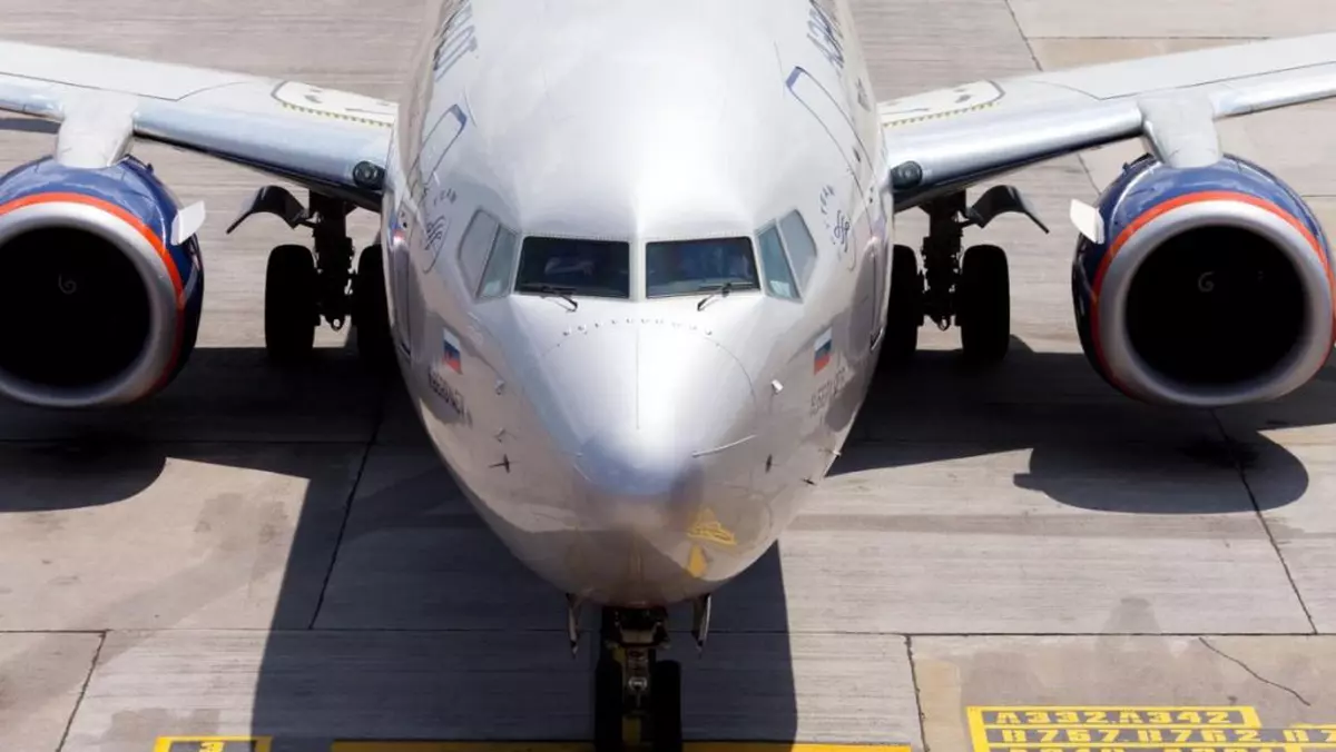Un avion Boeing de culoare argintie rulând pe o pistă a unui aeroport