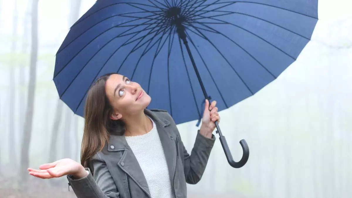 Femeie surprinsă în timp ce ține în mână o umbrelă și privește spre cer