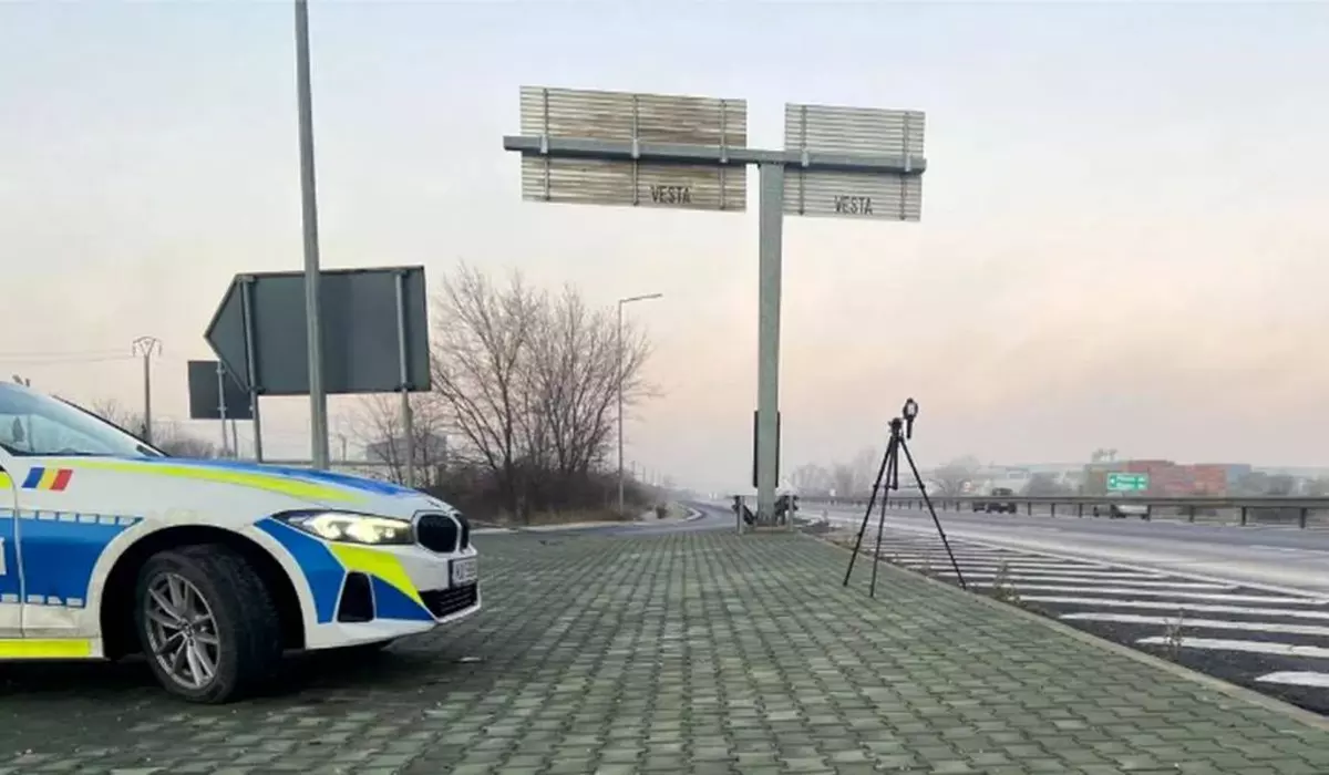 sistem radar pe trepied langa o masina de politie, in partea de sus sunt doua indicatoare rutiere de directie