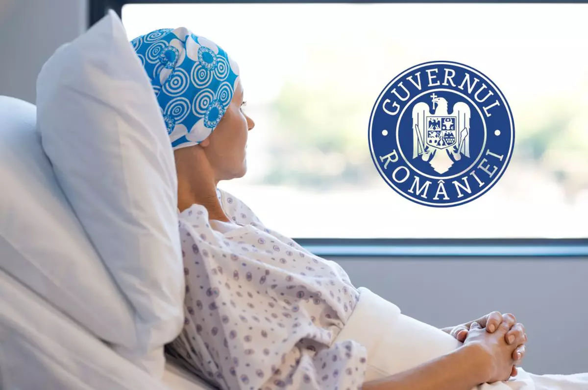in poza se observa o femeie care sta pe un pat de spital langa geam. ea poarta o boneta albastra pe cap si un halat alb de spital cu floricele
