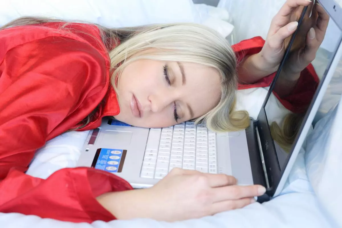Femeie blondă, obosită, care doarme cu capul pe tastatura laptopului în timpul zilei la birou.