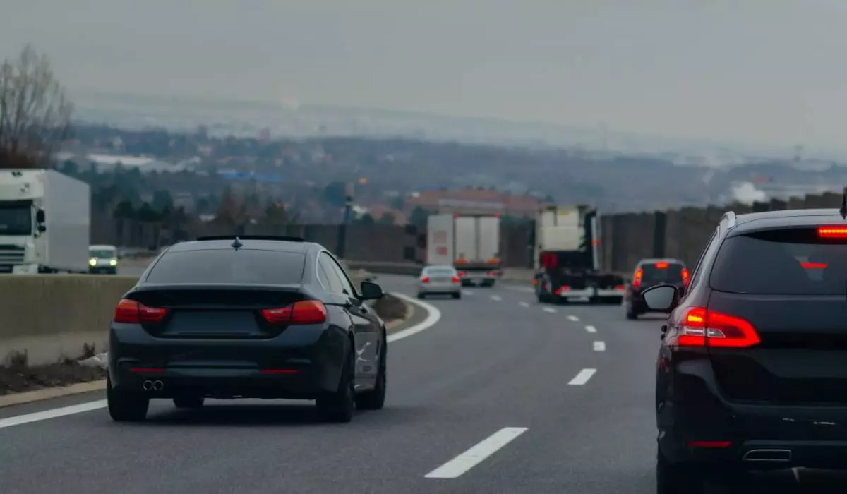 Autotradă aglomerată cu două benzi pe sens desparțite de un parapet.În prim plan sunt doua mașini negre, una care circulă pe banda doi, iar cealaltă pe banda unu.