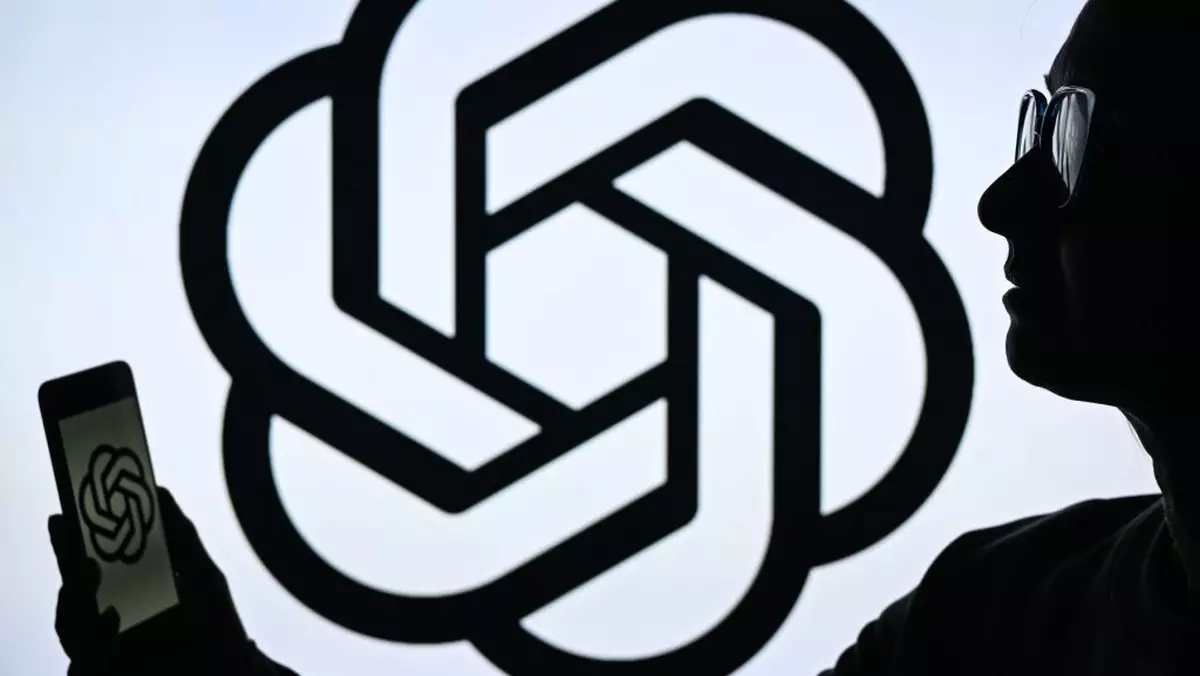 O femeie folosește un telefon mobil pe care este afișat logo-ul Open AI, același logo fiind vizibil pe un ecran de computer, în fundal