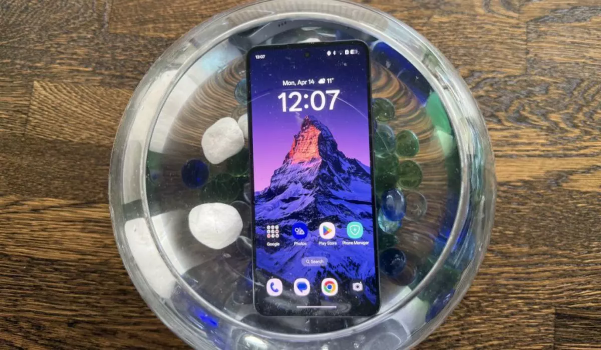 Un smartphone OPPO Reno13 F 5G, scufundat într-un bol plin cu apă și pietre colorate.