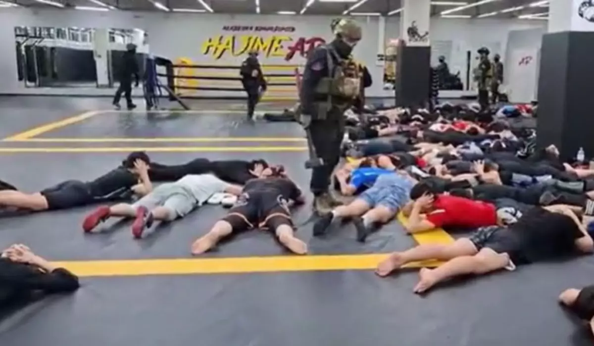 În imagine sunt ilustrați oameni întinși pe jos, în sala de sport, și polițiști care au intrat peste ei