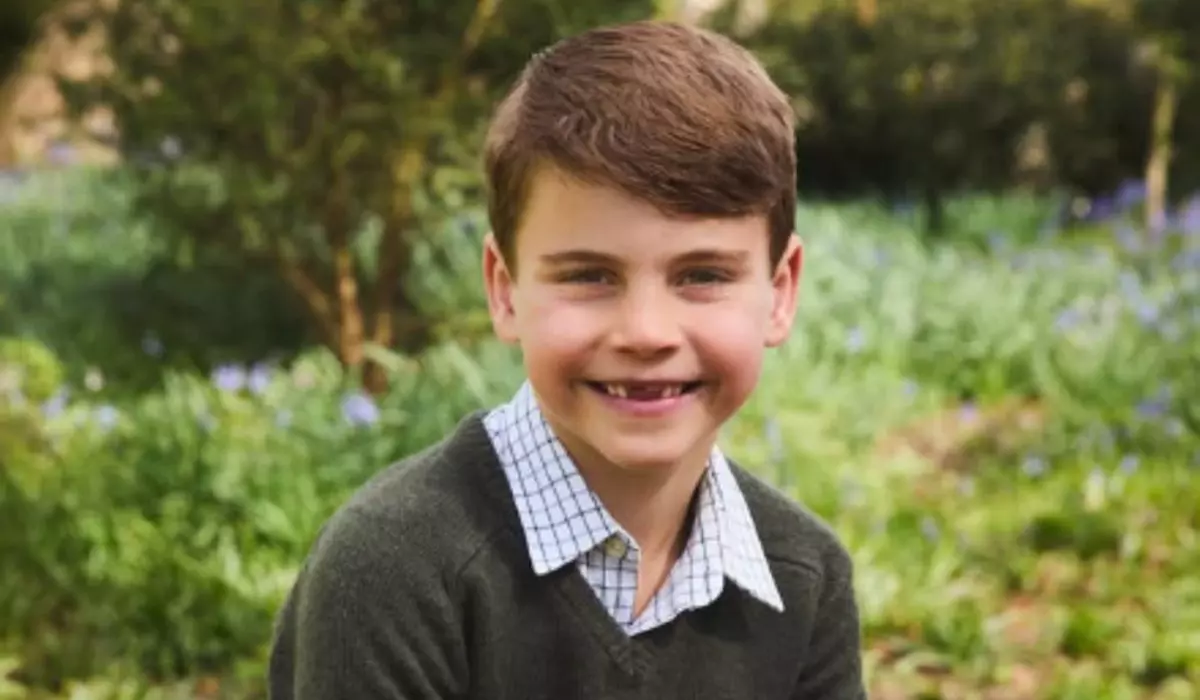 În imagine este ilustrat Prințul Louis stând pe un buștean, purtând o cămașă cu guler, un pulover verde și blugi