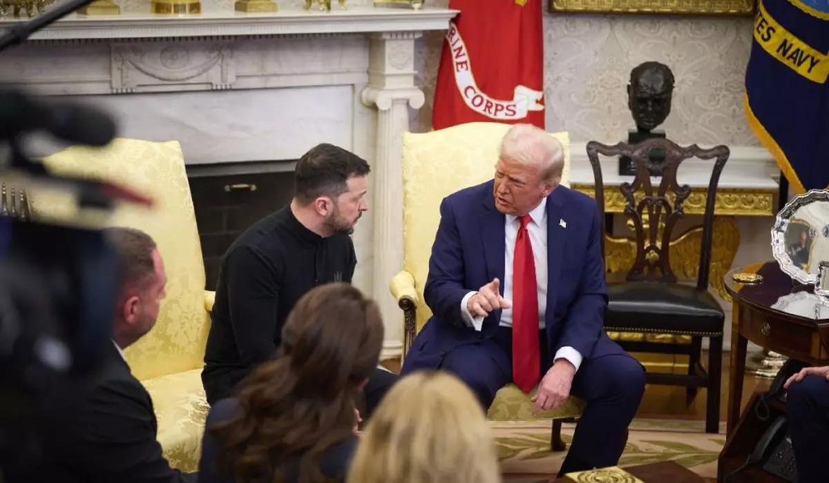 Doi bărbați stau pe două fotolii și discută. Cel din dreapta, Donald Trump, e în costum și are cravată roșie. Cel din stânga, Volodimir Zelenski, poartă un pulover închis la culoare