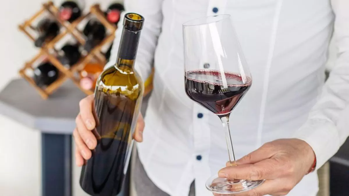 Pahar cu vin rosu și sticlă de vin în mâinile unei persoane îmbracată în alb