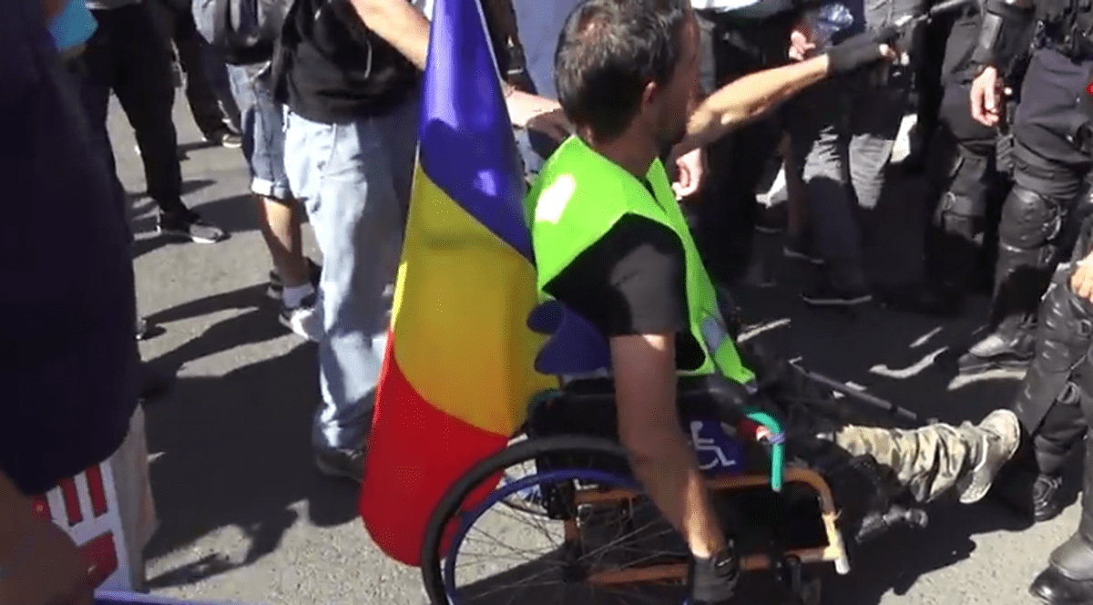 Un bărbat în scaun cu rotile a încercat să fure pistolul unui jandarm. Bărbatul în scaun cu rotile, cu un mic drapel național în spate, în momentul în care vrea să fure pistolul unui jandarm