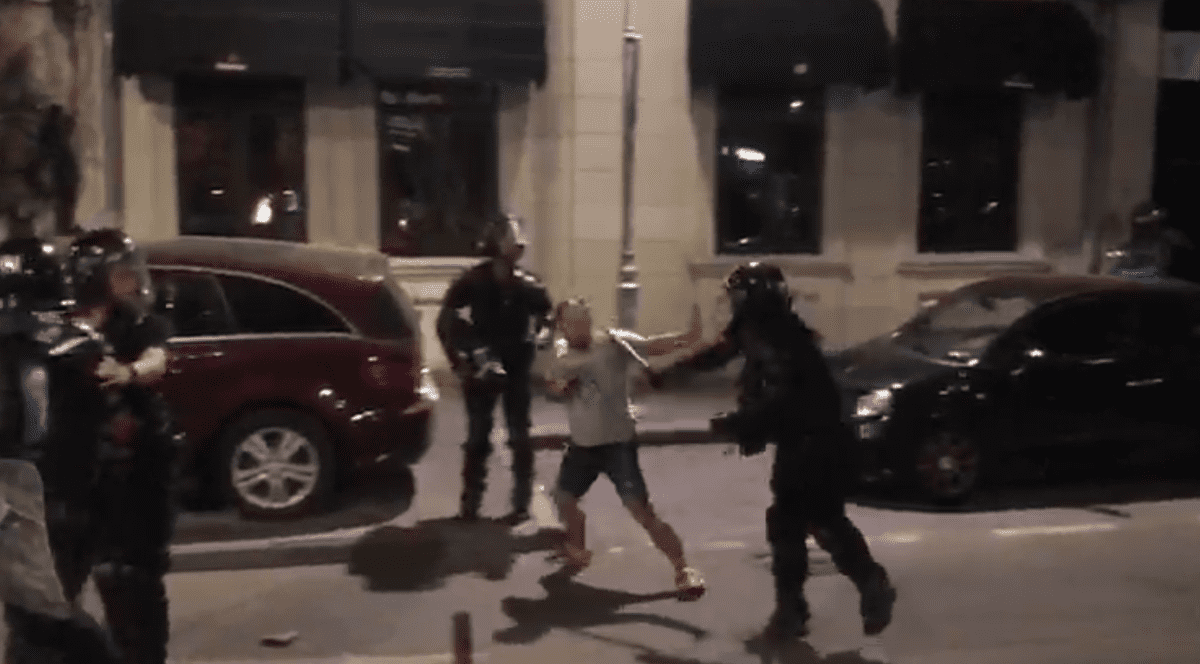 Un protestatar care mergea, cu mâinile ridicate, pe o stradă din apropierea Pieței Victoria este bătut cu bastonul de un jandarm, care îl lovește pe spate și în cap, apoi un alt jandar dă cu piciorul îl el.