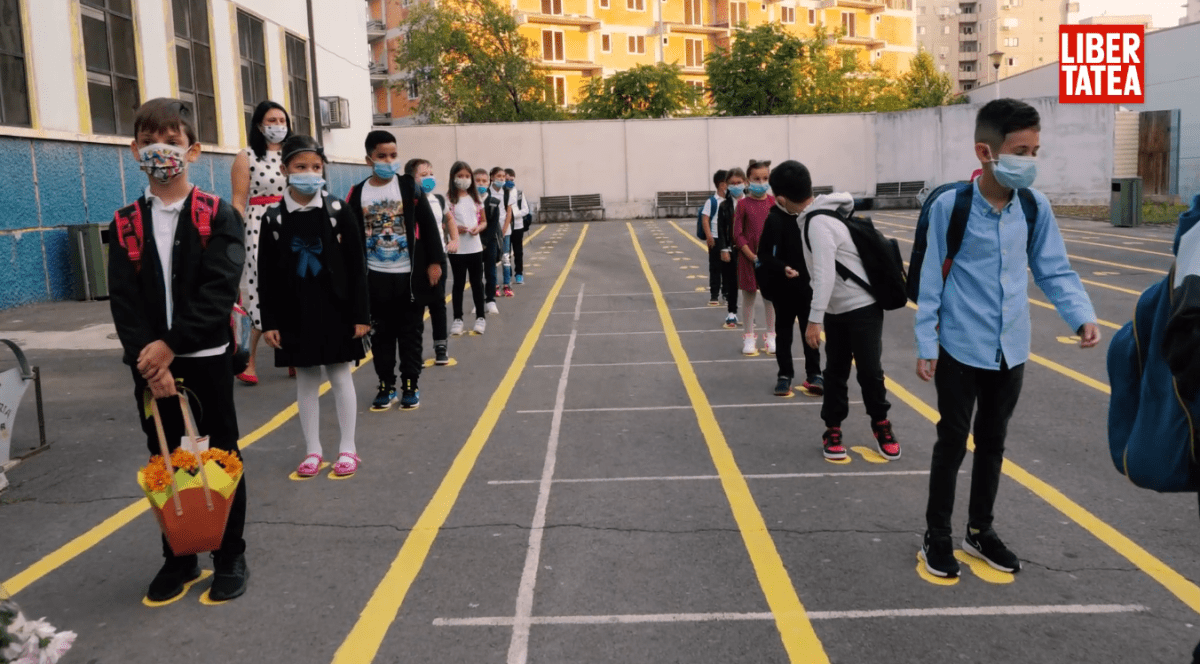 Mai muți elevi de la o școală din cartierul Ferentari din București stau aliniați în curtea școlii, cu măști pe față, pentru a intra în clase