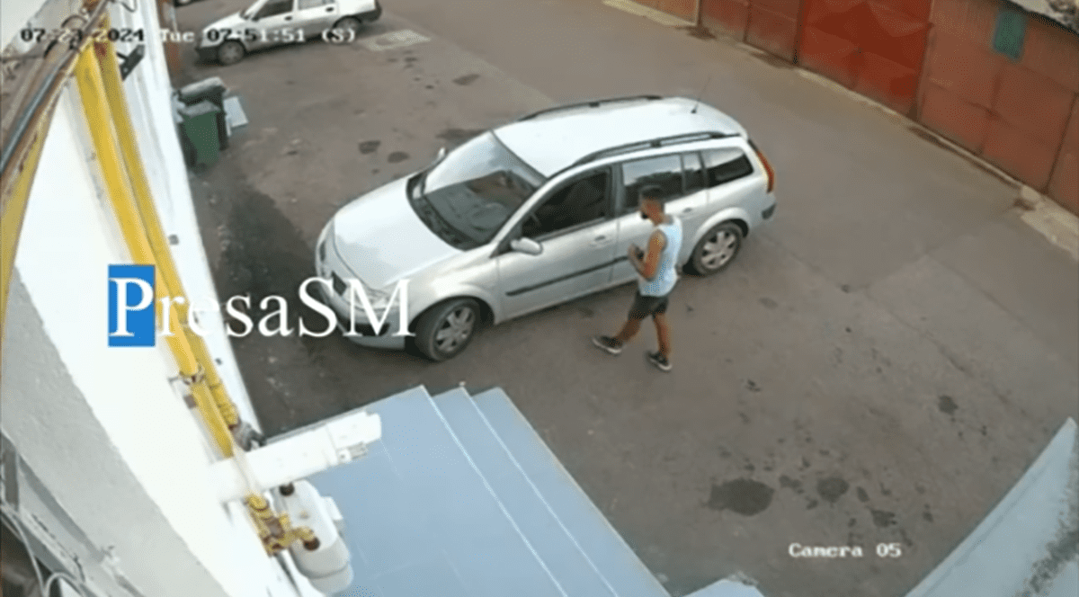 Un bărbat în tricou este suprins pe camerele de supraveghere când se uită la mașina pe care a furat-o ulterior din fața restaurantului