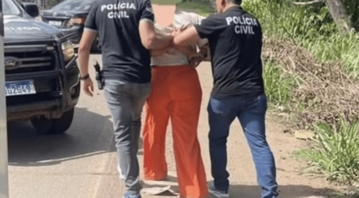 o femeie încătusată, care poartă pantaloni portocalii, este flncată de doi polițiști