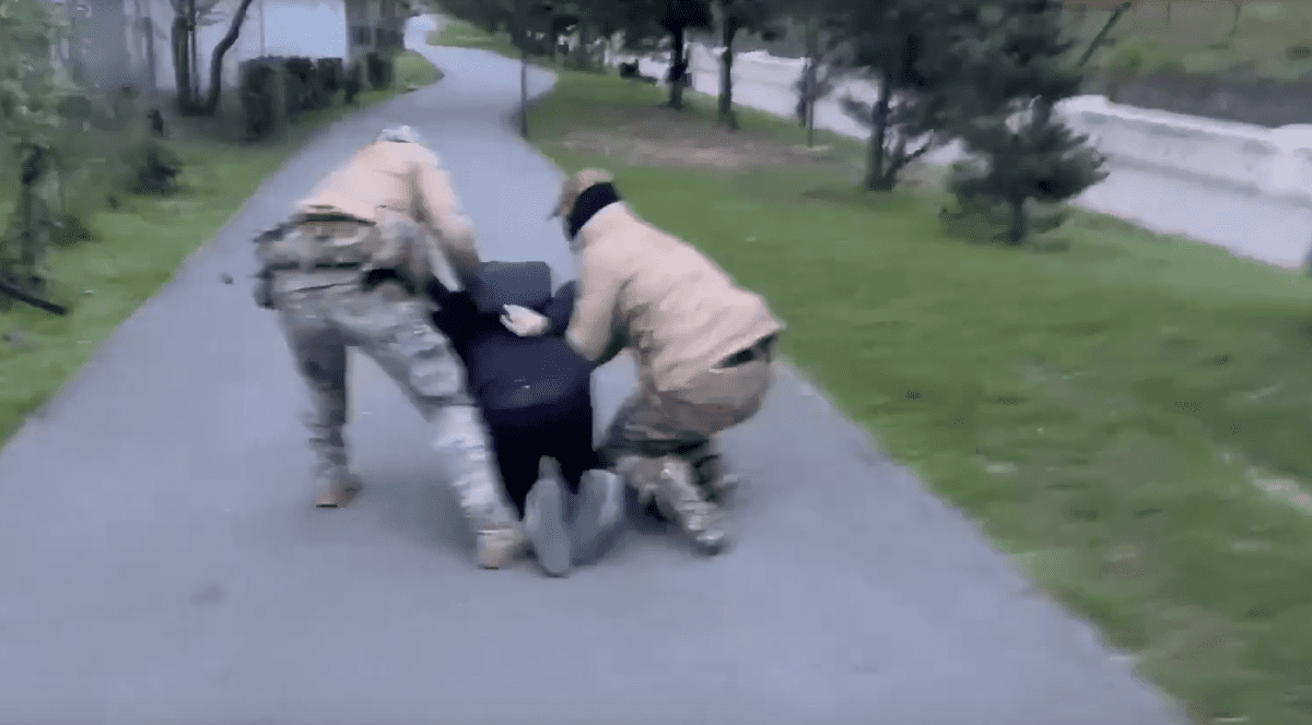 un bârbat, pus în genunchi pe asfalt de doi agenți ruși