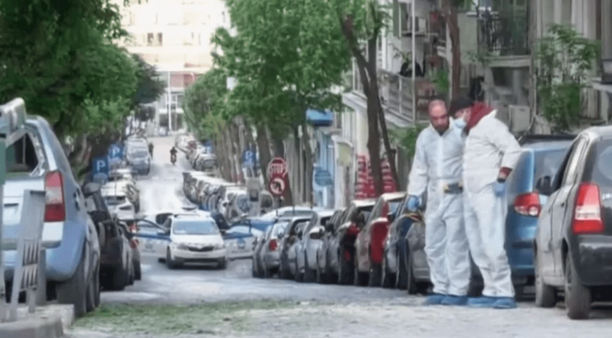doii polițiști în combinezoane albe, pe o stradă cu mașini parcate de o parte și de alta, fac cercetarea la locul exploziei