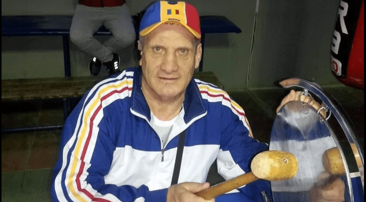 Titi Tudor Prosop, îmbrăcat în trening și cu o șapcă tricoloră pe cap stă pe un scaun și bate gongul într-o sală de box din Ploiești, aprile 2020