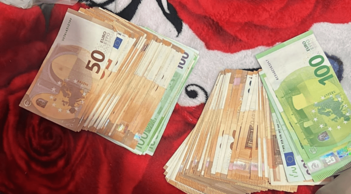 Două teancuri de bancnote de 50 și 100 de euro lână un fes roșu stau pe o canapea