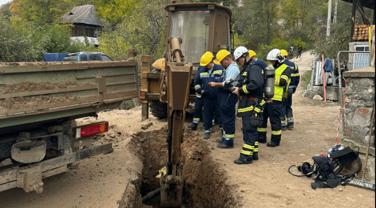 Mai mulți muncitori stau lângă un excavator care a lovit o conductă de gaze în Băile Olănești, 23 octombrie 2025