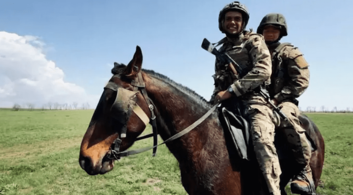 Doi militari ruși cu puștile la spate stau pe un cal, septembrie 2025