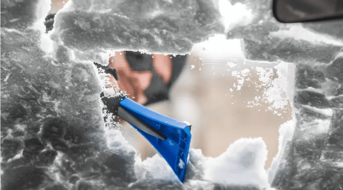 un bărbat curăță cu o racletă parbrizul înghețat al mașiinii