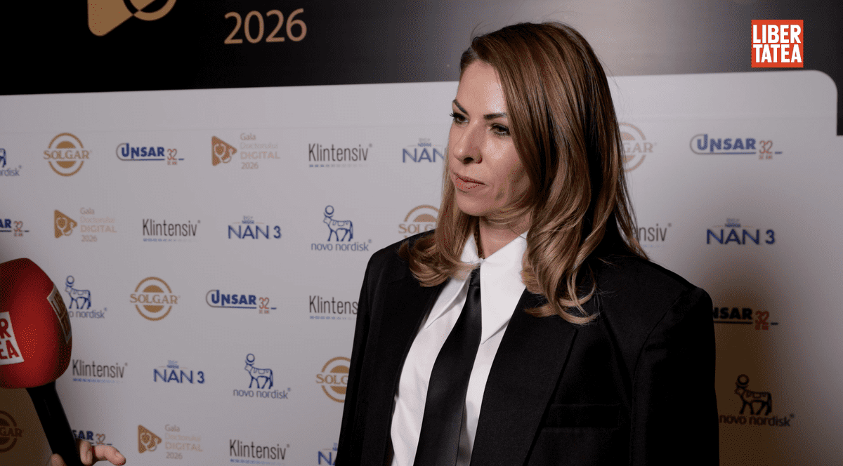 Dr. Anca Sultan, medic specialist obstetrică-ginecologie, a vorbit la Gala Doctorului Digital 2026, îmbrăcată cu o cămașă albă, un sacou negru și o cravată neagră, pe un fundal cu un panou alb.