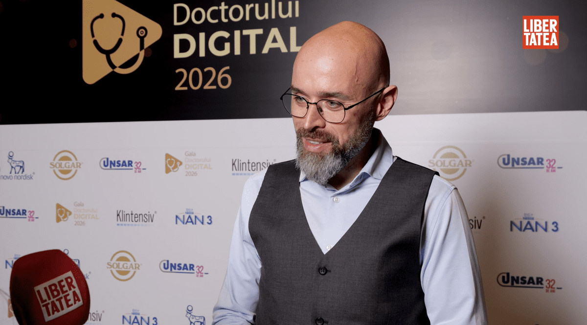 Dr. Răzvan Vintil, medic specialist în medicină de familie, îmbrăcat cu o cămașă albă și o vestă gri, pe un fundal cu un panou alb și negru.