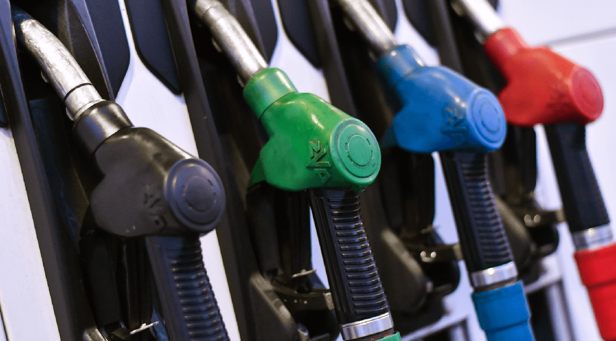 Imaginea surprinde un rând de patru pistoane de alimentare cu combustibil de culori diferite - negru, verde, albastru și roșu - așezate în suporturi, la pompă, într-o benzinărie/