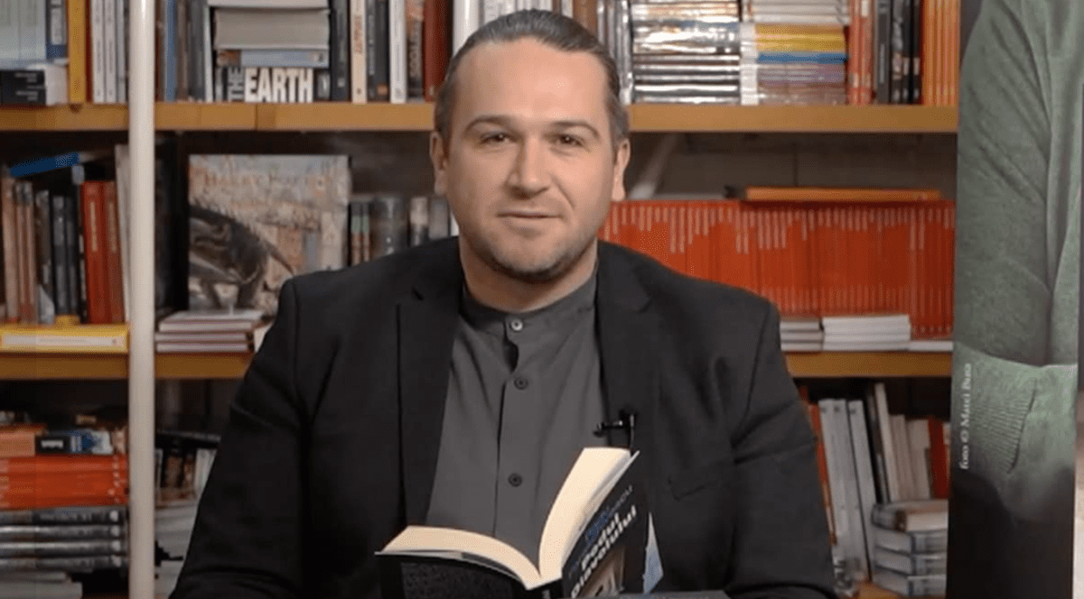 Sebastian Zachmnn ține în mână o carte, având pe fundal o bibliotecă