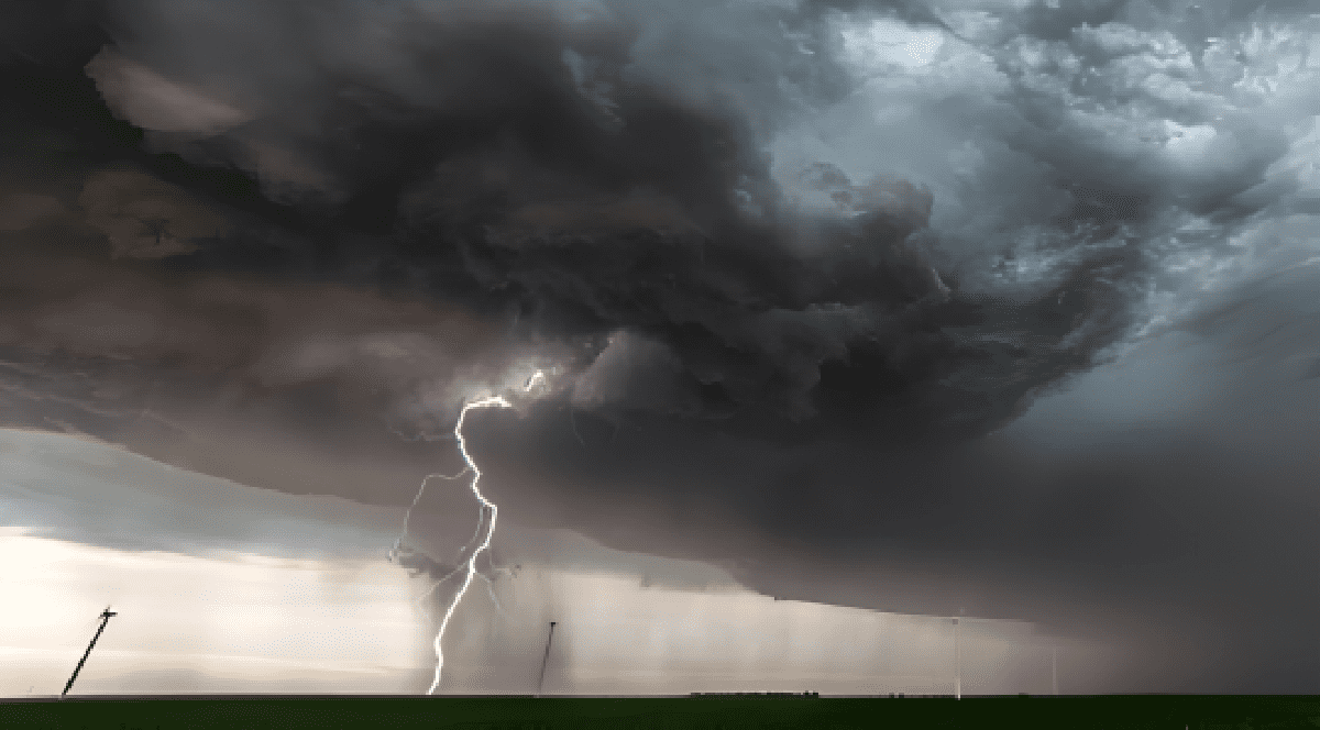 Imaginea surprinde un fenomen meteorologic extrem, înfățișând un fulger care lovește pământul sub o formațiune masivă de nori de furtună de tip supercelulă, deasupra unui câmp deschis.