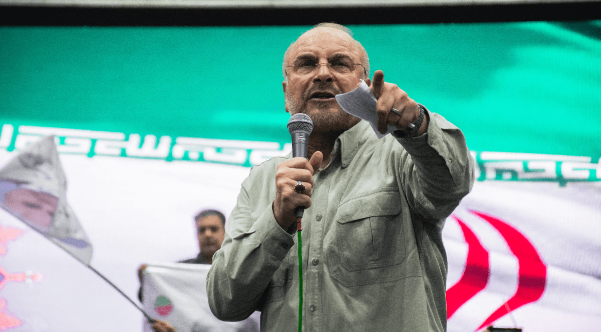 Imaginea îl înfățișează pe politicianul iranian Mohammad Bagher Ghalibaf vorbind la un microfon și arătând cu degetul înainte, având în fundal steagul Iranului.