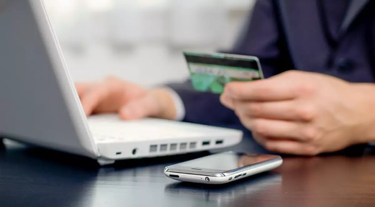 De la open source la open banking. O companie suedeză vrea să revoluționeze plățile interconectând mii de bănci. Bărbat care stă cu cardul în mână în fața laptopului