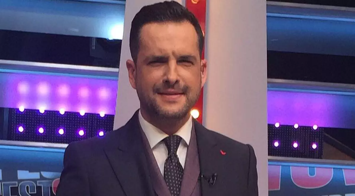 Mădălin Ionescu, îmbrăcat la costum și zâmbitor, în platoul unei emisiuni de televiziune