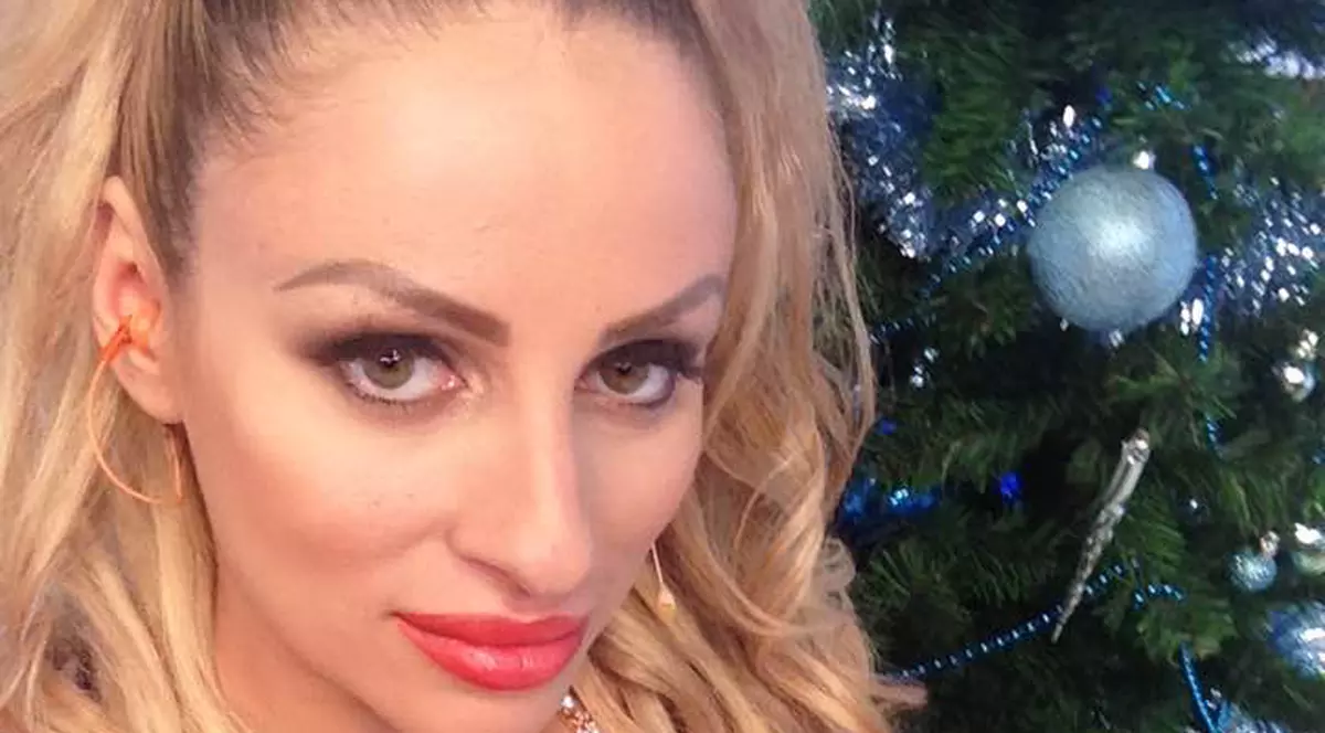 Sanziana Buruiană, îmbrăcată într-o rochie roșie cu decolteu adânc, pozează lângă bradul de Crăciun