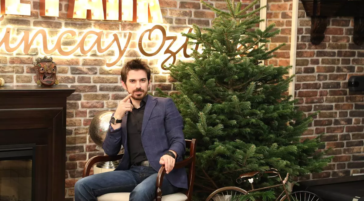 Tuncay Ozturk stă așezat pe un scaun, lângă bradul de Crăciun