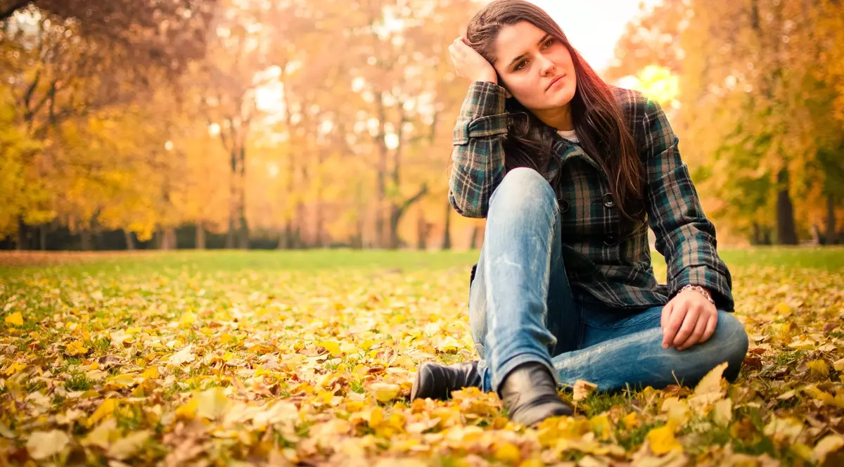 Stresul din viaţa profesională e principala cauză a depresiei. O tânără deprimată, care stă pe niște frunze galbene... toamna