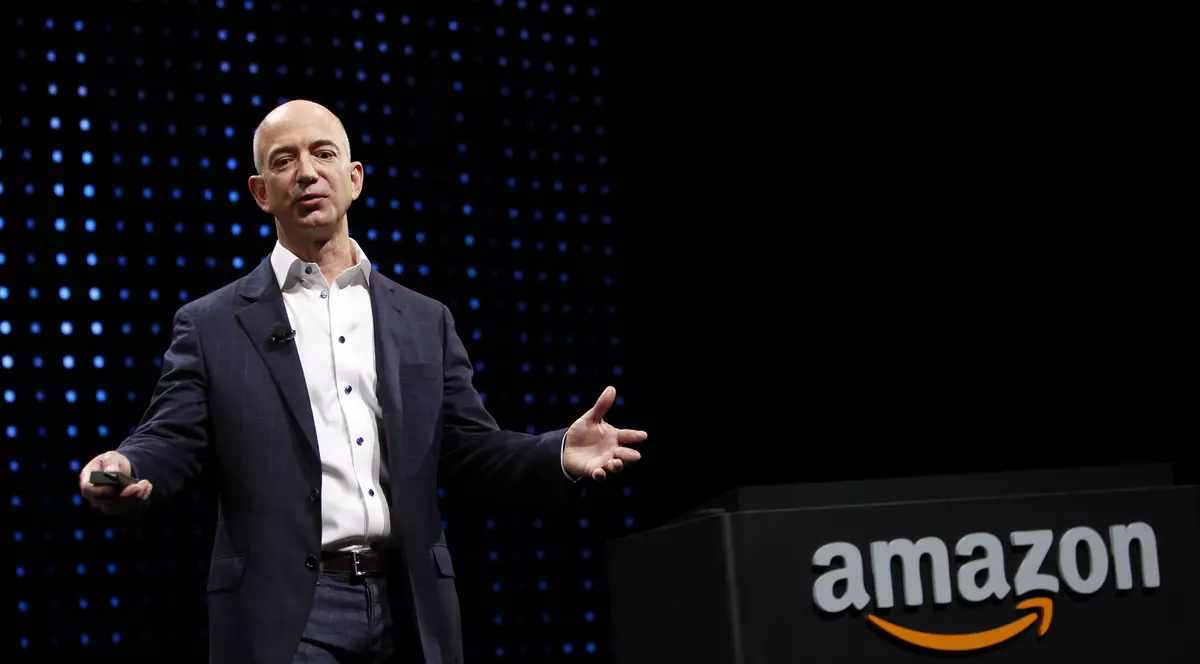 Amazon cumpără Ring, o companie care produce sonerii inteligente și camere de securitate dotate cu asistentul virtual Alexa, cu un miliard de dolari. Jeff Bezos, fondatorul și șeful Amazon, pe o scenă cu logo-ul Amazon pe fundal negru