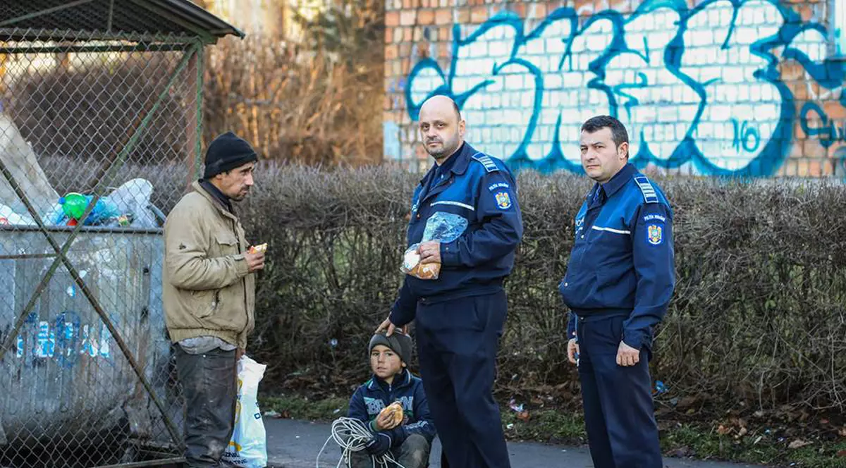 Doi poliţişti din Braşov, fotografiați hrănind nişte oameni ai străzii care scormoneau prin gunoaie