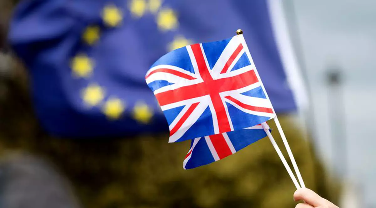 Numărul românilor care emigrează în Marea Britanie a scăzut. Un om flutură dou steaguri mici ale Marii Britanie, în timp ce pe fundal se observă un drapel mare al UE