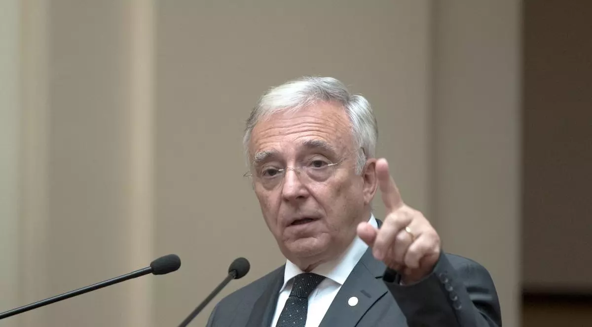 BNR prezintă raportul trimestrial asupra inflaţiei. Mugur Isărescu, la un pupitru, cu mâna stângă ridicată și degetul arătător în aer