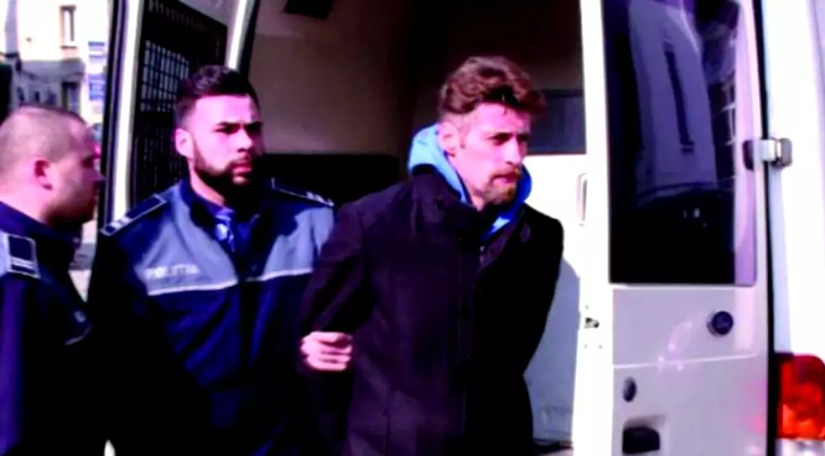 În arest, asasinul din Brașov Florin Buliga, citește Biblia, își scrie memoriile. Florin buliga încadrat de doi agenți lângă duba poliției