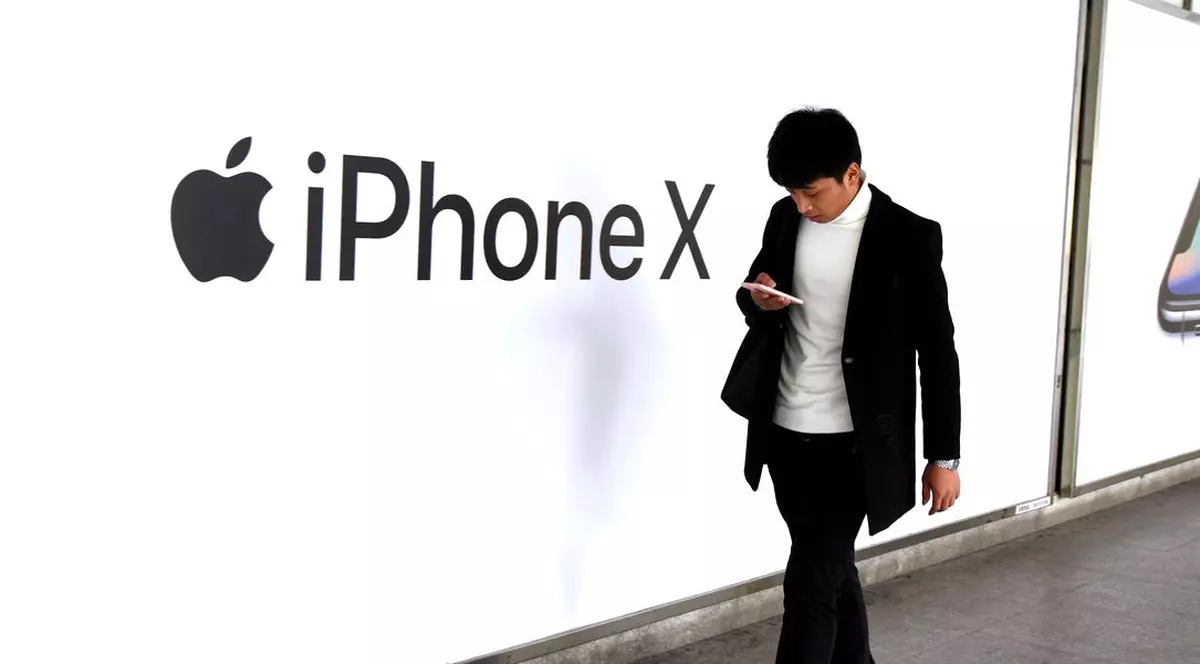 Japonia acuză Apple de comportament anticoncurențial. Un om trece prin fața unui perete pe care scrie iPhone X